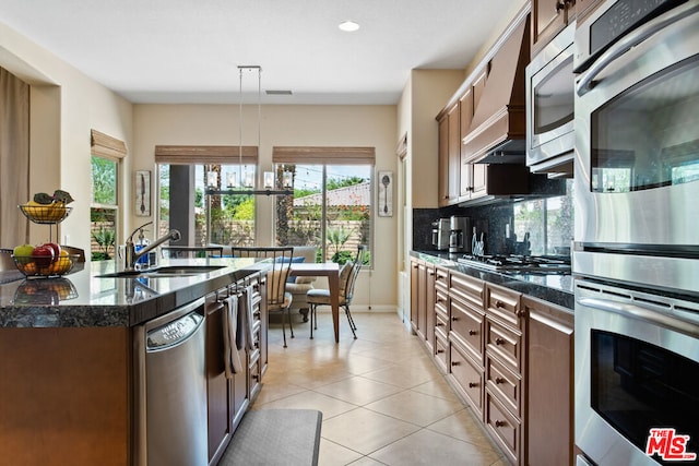 kitchen featuring wall chimney range hood, pendant lighting, decorative backsplash, sink, and appliances with stainless steel finishes