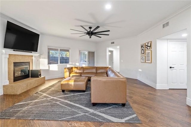 living room featuring a tile fireplace, hardwood / wood-style flooring, ceiling fan, and ornamental molding