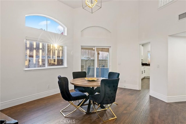 dining room featuring dark wood-type flooring, a wealth of natural light, and a towering ceiling