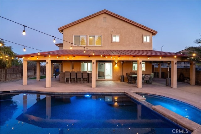 pool at dusk with an in ground hot tub, a patio area, and exterior bar