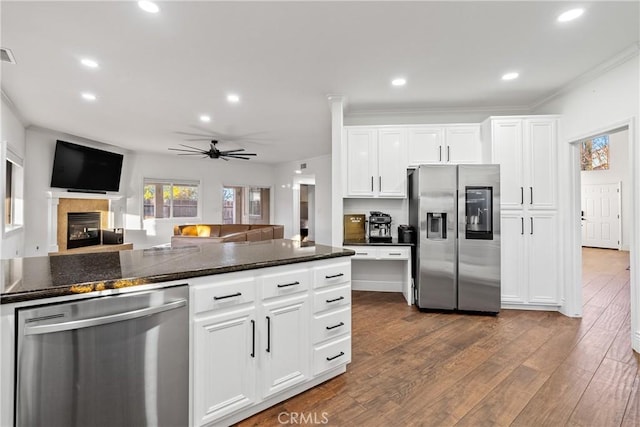 kitchen featuring white cabinets, appliances with stainless steel finishes, dark stone countertops, ceiling fan, and a tiled fireplace