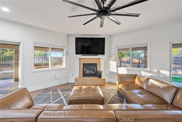 living room with ceiling fan, wood-type flooring, a tiled fireplace, and a healthy amount of sunlight