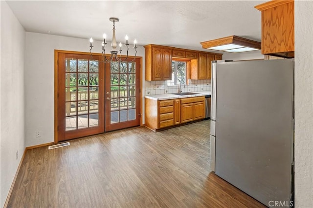 kitchen with pendant lighting, appliances with stainless steel finishes, hardwood / wood-style floors, sink, and backsplash