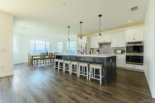 kitchen with hanging light fixtures, appliances with stainless steel finishes, an island with sink, and white cabinetry