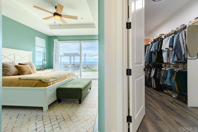 bedroom featuring hardwood / wood-style flooring, ceiling fan, access to exterior, and a raised ceiling