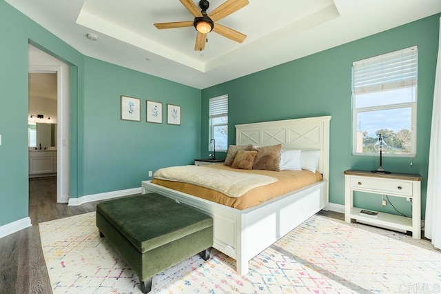 bedroom featuring multiple windows, wood-type flooring, ensuite bathroom, ceiling fan, and a tray ceiling