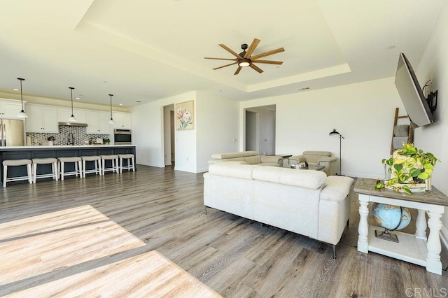 living room with a raised ceiling, ceiling fan, and dark wood-type flooring