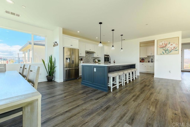 kitchen with decorative light fixtures, white cabinets, stainless steel appliances, and a center island with sink