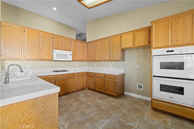 kitchen featuring kitchen peninsula, tile counters, white appliances, light tile patterned flooring, and sink