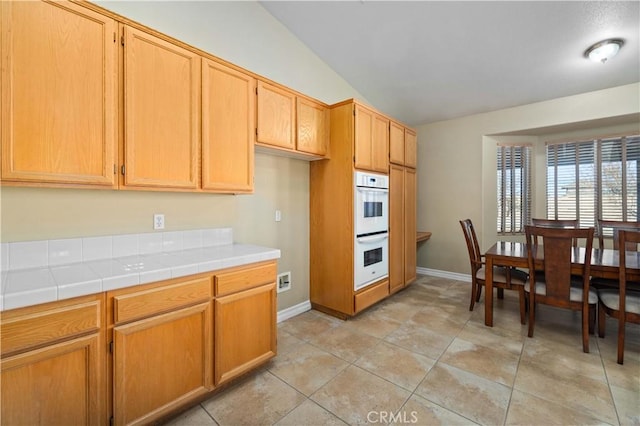 kitchen featuring light tile patterned floors, double oven, tile counters, and vaulted ceiling