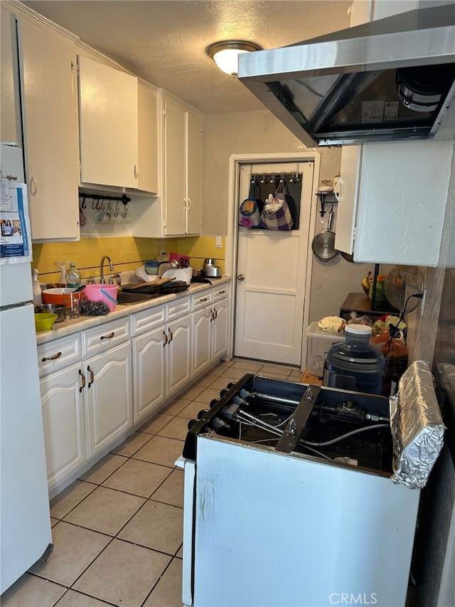 kitchen featuring range hood, light tile patterned floors, gas range oven, white cabinets, and white refrigerator