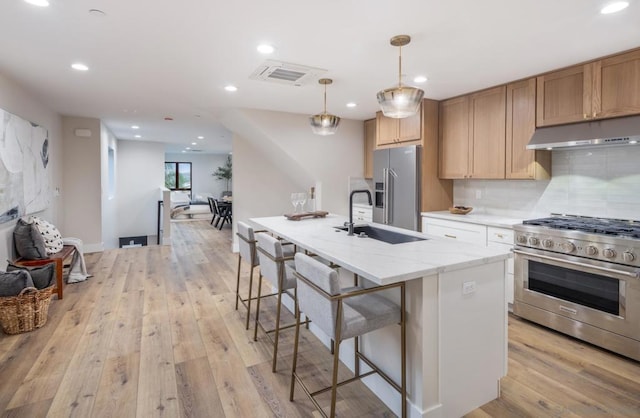 kitchen with pendant lighting, sink, high end appliances, light wood-type flooring, and an island with sink