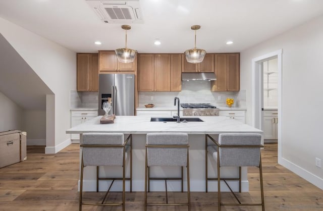 kitchen featuring stainless steel refrigerator with ice dispenser, stove, light wood-type flooring, and a kitchen island with sink