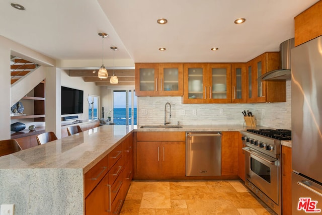 kitchen featuring stainless steel appliances, a kitchen breakfast bar, light stone countertops, wall chimney exhaust hood, and sink