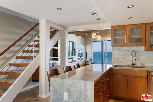 kitchen with a kitchen breakfast bar, light stone countertops, pendant lighting, a water view, and sink