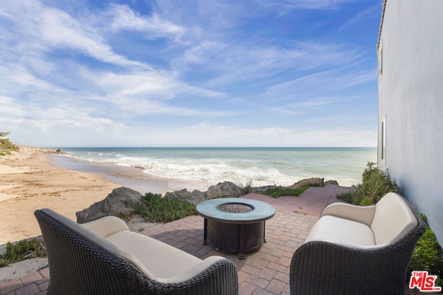 view of patio with a beach view, a fire pit, and a water view