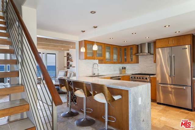 kitchen featuring backsplash, hanging light fixtures, wall chimney exhaust hood, high quality appliances, and sink