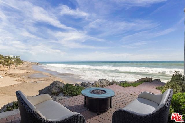 view of patio / terrace with a view of the beach, a water view, and an outdoor fire pit