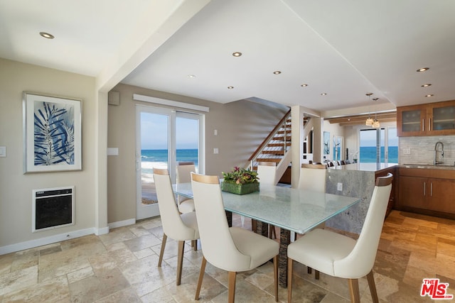 dining area with heating unit, a water view, and sink