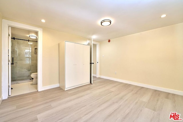 unfurnished bedroom featuring ensuite bathroom, a closet, and light hardwood / wood-style flooring