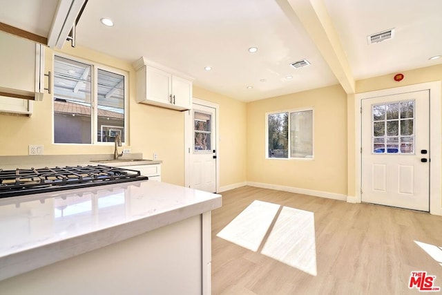 kitchen with white cabinetry, beam ceiling, light hardwood / wood-style flooring, light stone counters, and sink