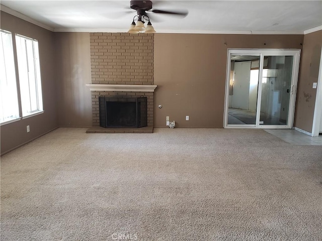 unfurnished living room featuring ceiling fan, a brick fireplace, crown molding, and carpet flooring