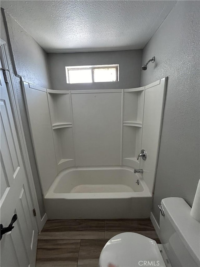 bathroom with toilet, wood-type flooring, a textured ceiling, and washtub / shower combination