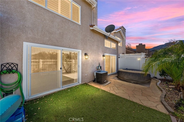 back house at dusk featuring central AC unit and a patio area