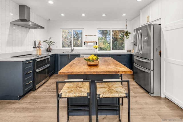 kitchen with wall chimney range hood, sink, a breakfast bar, appliances with stainless steel finishes, and white cabinets