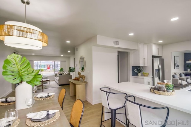 kitchen with stainless steel fridge with ice dispenser, light hardwood / wood-style floors, backsplash, pendant lighting, and white cabinets