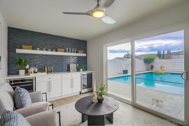 living room with light hardwood / wood-style floors, beverage cooler, indoor bar, and ceiling fan