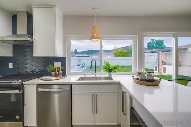 kitchen with decorative backsplash, sink, white cabinetry, appliances with stainless steel finishes, and wall chimney exhaust hood