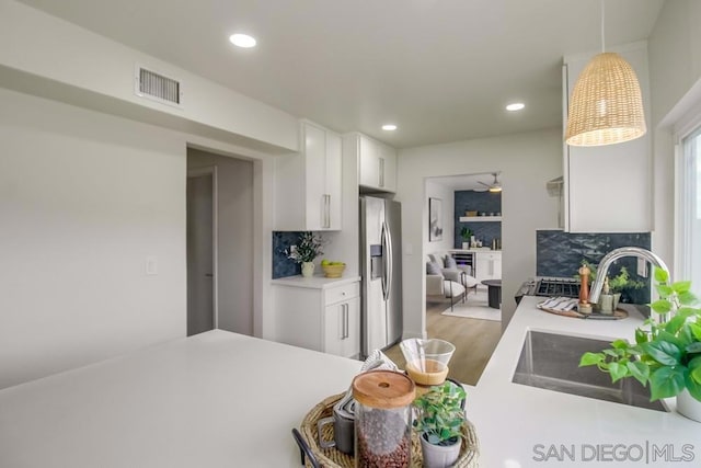 kitchen with decorative backsplash, sink, hanging light fixtures, stainless steel fridge with ice dispenser, and white cabinets