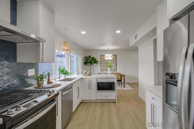 kitchen featuring white cabinets, wall chimney exhaust hood, stainless steel appliances, sink, and hanging light fixtures