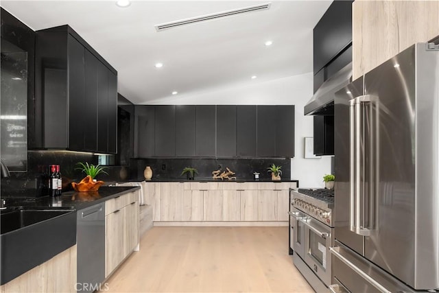 kitchen featuring lofted ceiling, decorative backsplash, high end appliances, light wood-type flooring, and light brown cabinets