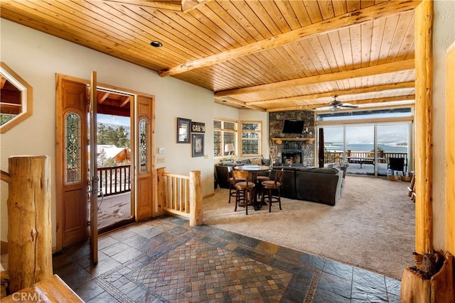 carpeted living room with ceiling fan, beamed ceiling, a stone fireplace, and wood ceiling