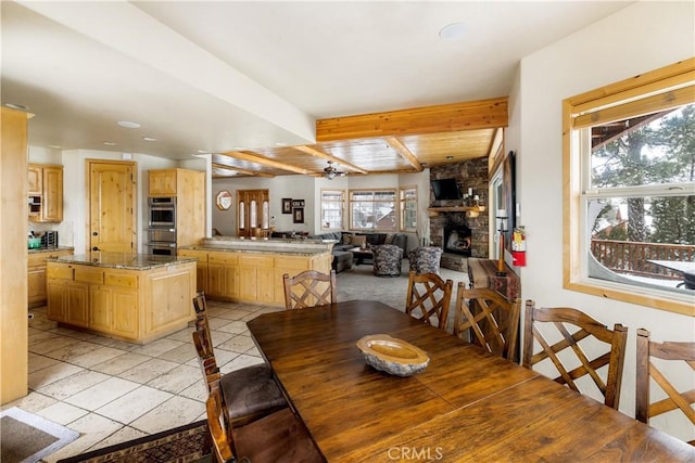 tiled dining area featuring ceiling fan, wooden ceiling, beam ceiling, and a fireplace