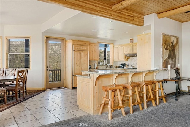 kitchen featuring tasteful backsplash, kitchen peninsula, wood ceiling, a kitchen breakfast bar, and light brown cabinets