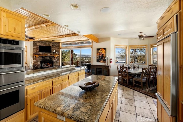 kitchen with paneled refrigerator, ceiling fan, dark stone countertops, a fireplace, and a kitchen island