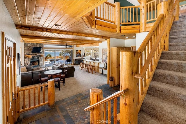 dining space with beamed ceiling, a stone fireplace, ceiling fan, wooden ceiling, and dark carpet