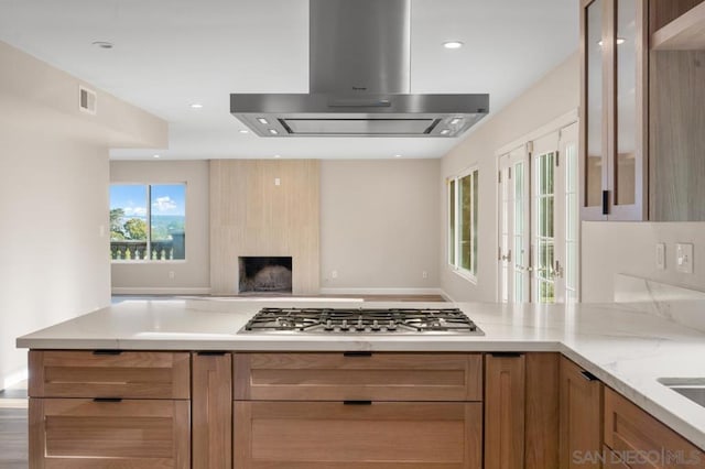 kitchen with light stone countertops, stainless steel gas stovetop, and range hood