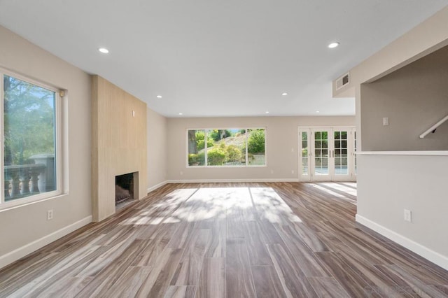 unfurnished living room with light hardwood / wood-style floors, a large fireplace, and french doors