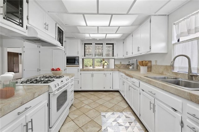 kitchen featuring stainless steel microwave, sink, light tile patterned flooring, white cabinetry, and white range with gas stovetop