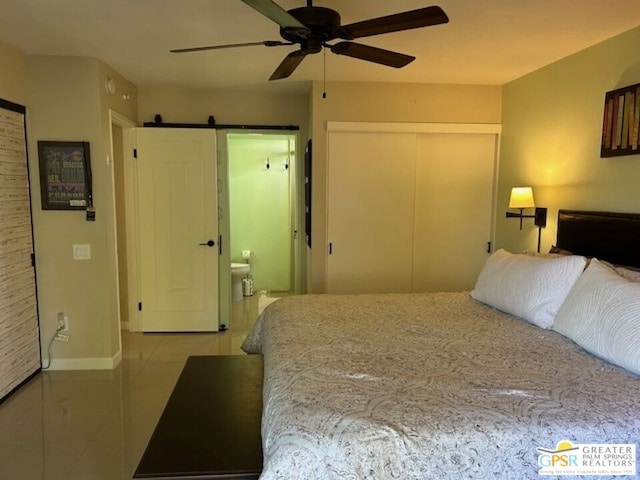 tiled bedroom featuring ceiling fan, a closet, ensuite bath, and a barn door