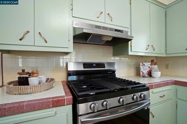 kitchen with decorative backsplash, stainless steel gas range oven, tile countertops, and green cabinets