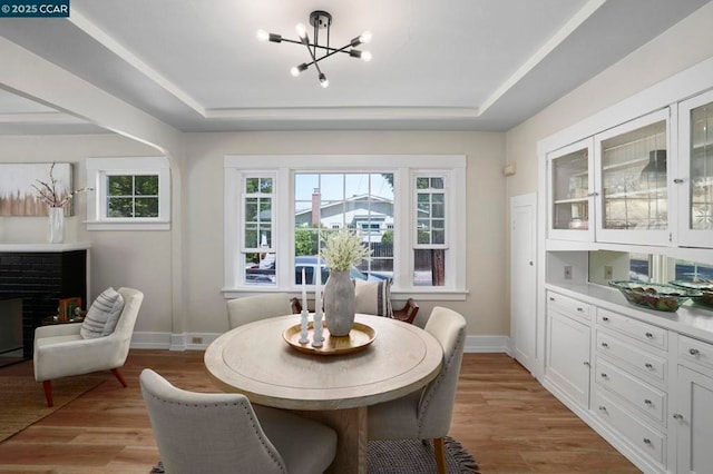 dining room with a chandelier, a raised ceiling, a brick fireplace, and light wood-type flooring