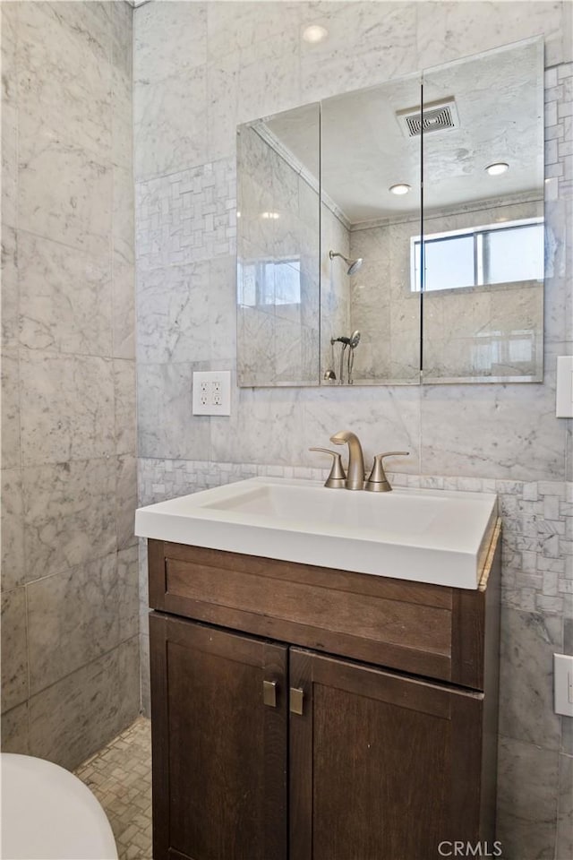 bathroom featuring toilet, vanity, tile walls, and a shower