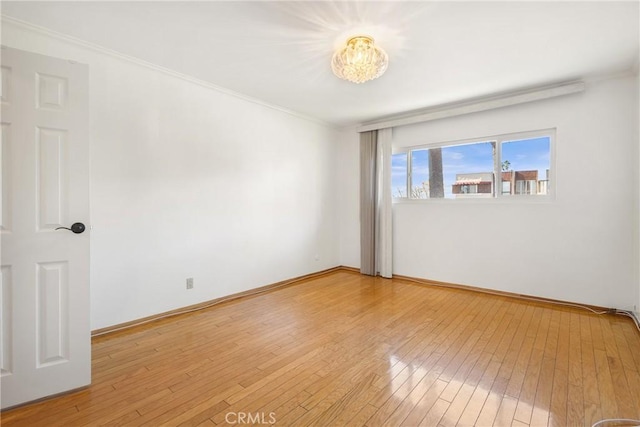 spare room with crown molding, a chandelier, and light wood-type flooring