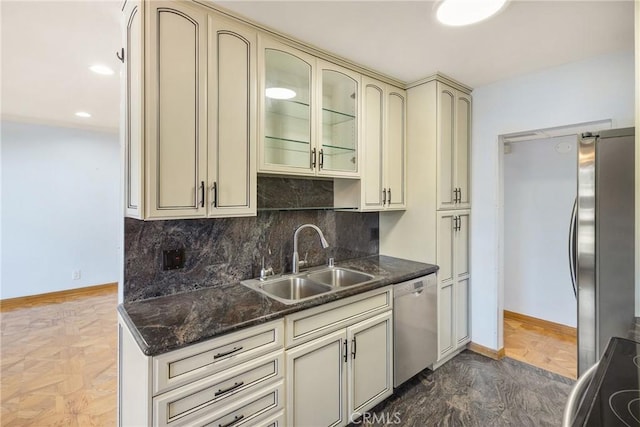 kitchen with cream cabinetry, appliances with stainless steel finishes, tasteful backsplash, dark stone counters, and sink