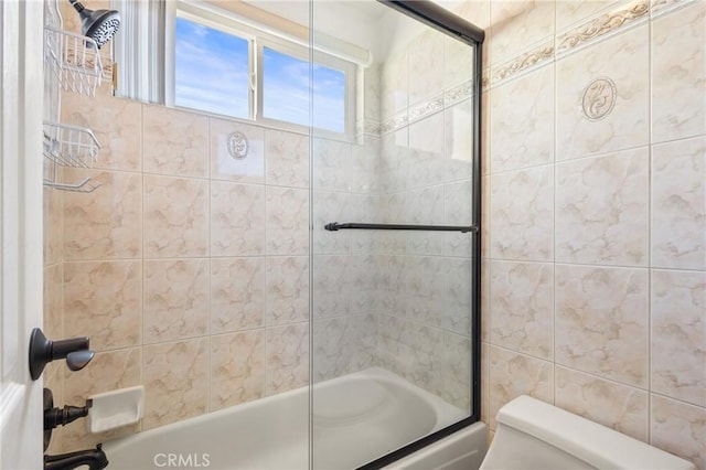 bathroom featuring tile walls, shower / bath combination with glass door, and toilet